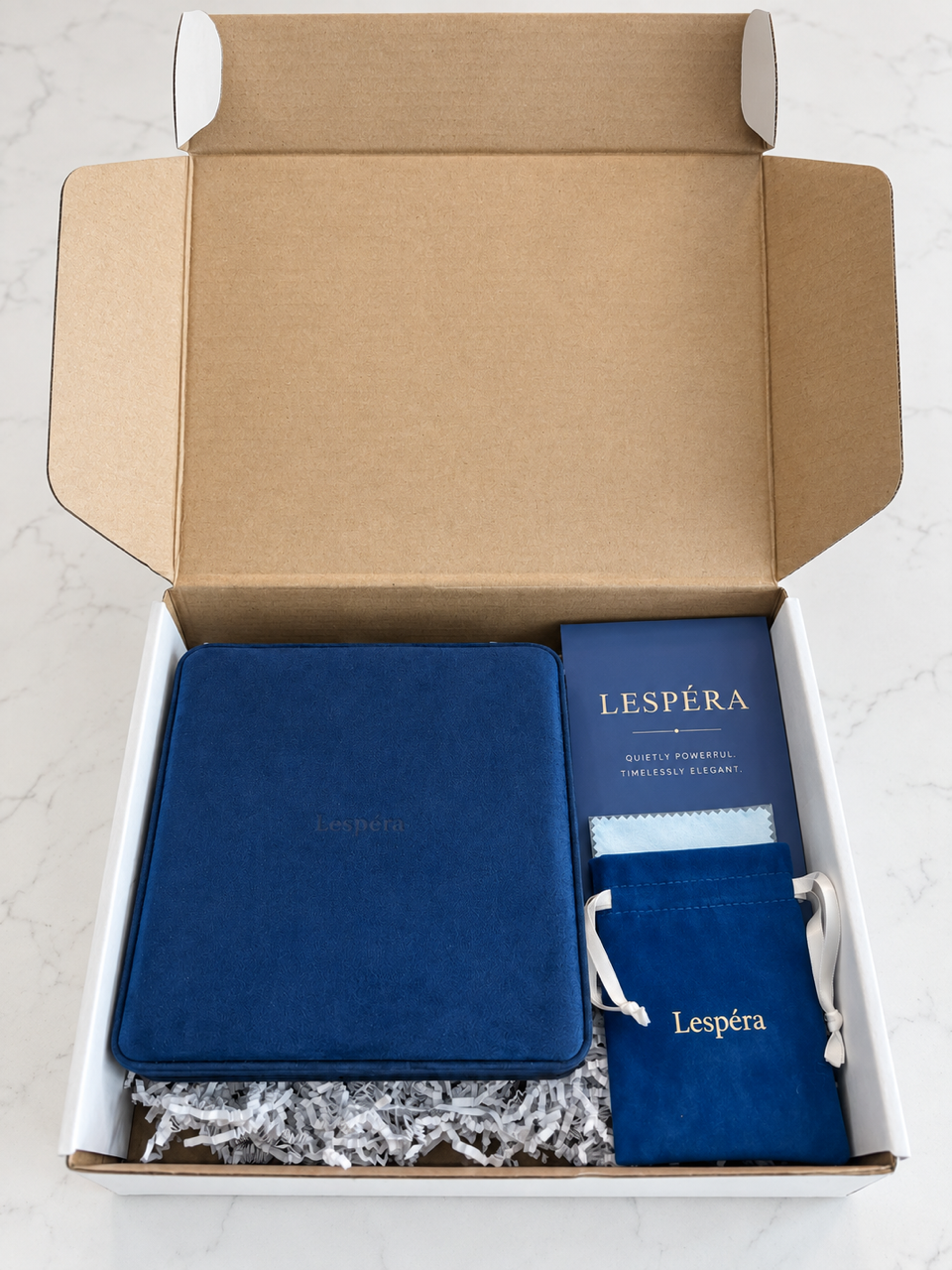 Un écrin cadeau Lespéra ouvert montrant un coffret en velours bleu marine, une carte d'entretien et une pochette à cordon