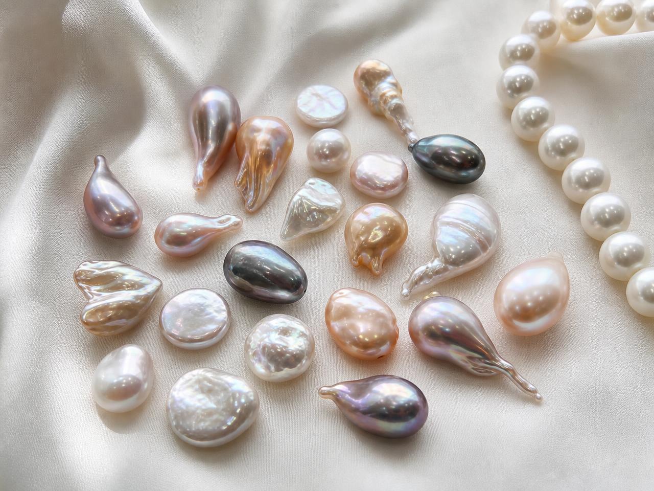 Baroque pearls with organic freeform shapes arranged beside classic round white pearls on ivory silk